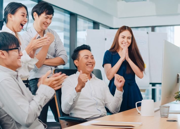 Millennial group of young businesspeople Asia businessman and businesswoman celebrate giving five after dealing feeling happy and signing contract or agreement at meeting room in small modern office.